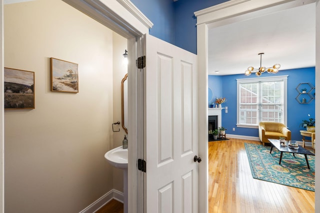 bathroom featuring a fireplace with flush hearth, baseboards, wood-type flooring, and a chandelier