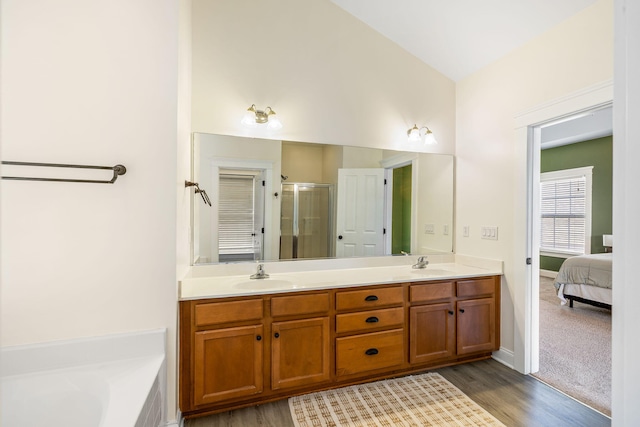 ensuite bathroom featuring double vanity, a shower stall, a sink, and wood finished floors