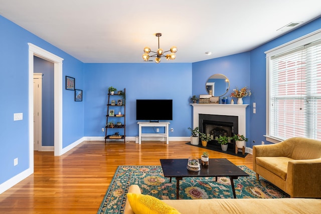 living room featuring a chandelier, baseboards, a fireplace with flush hearth, wood finished floors, and visible vents