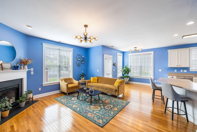 living area featuring baseboards, a fireplace with flush hearth, light wood finished floors, and a chandelier