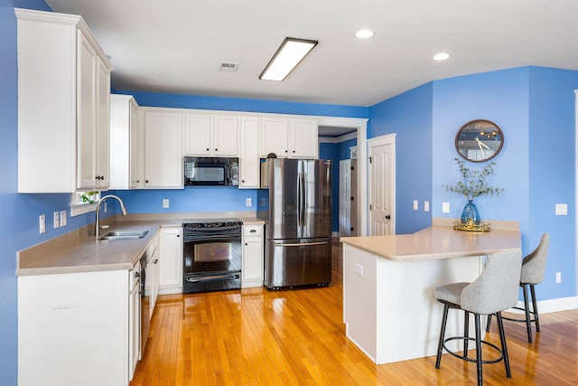 kitchen with white cabinets, a sink, a kitchen breakfast bar, a peninsula, and black appliances
