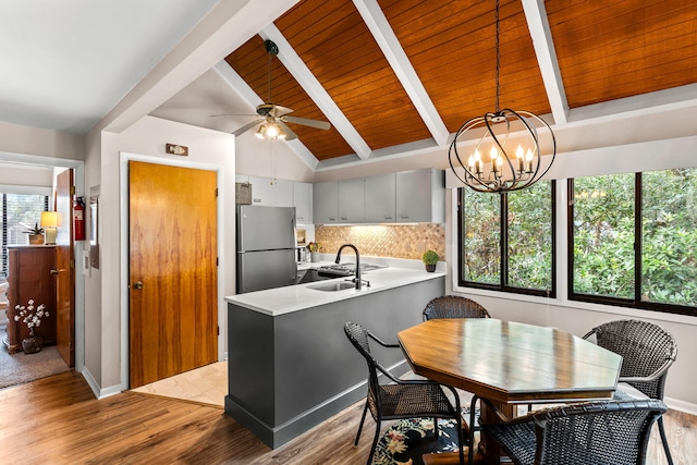 kitchen featuring lofted ceiling with beams, ceiling fan with notable chandelier, tasteful backsplash, stainless steel fridge, and kitchen peninsula