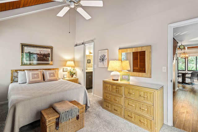 carpeted bedroom featuring ceiling fan with notable chandelier, a barn door, connected bathroom, and lofted ceiling