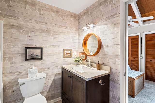 bathroom featuring ceiling fan, wooden walls, vanity, and toilet