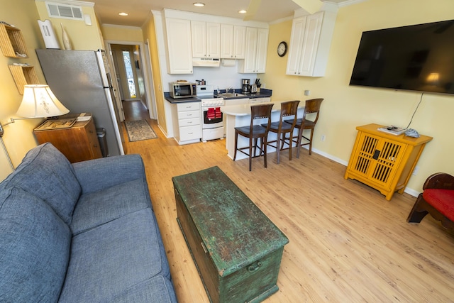 living room featuring baseboards, visible vents, light wood-style flooring, recessed lighting, and ornamental molding