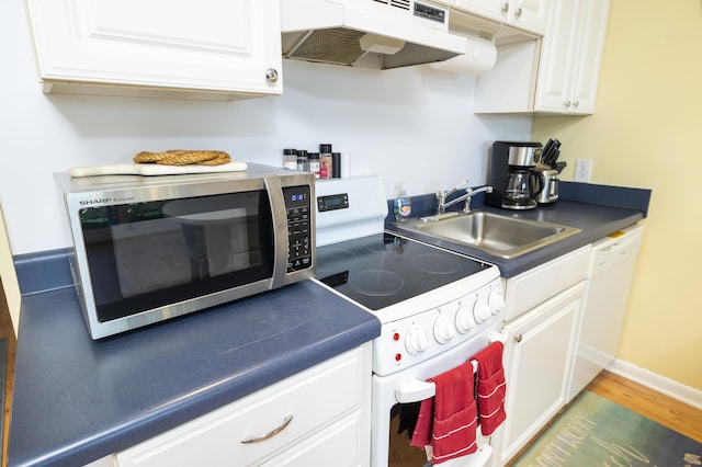 kitchen with dark countertops, under cabinet range hood, white cabinets, white appliances, and a sink