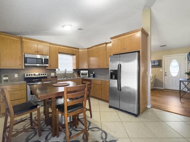 kitchen with light tile patterned floors, lofted ceiling, a sink, appliances with stainless steel finishes, and tasteful backsplash