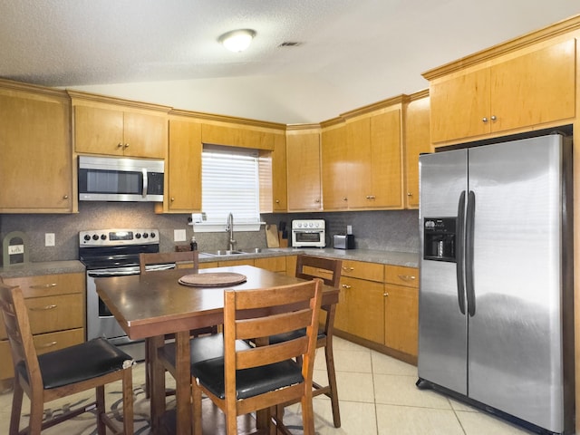 kitchen with stainless steel appliances, lofted ceiling, decorative backsplash, light tile patterned flooring, and a sink