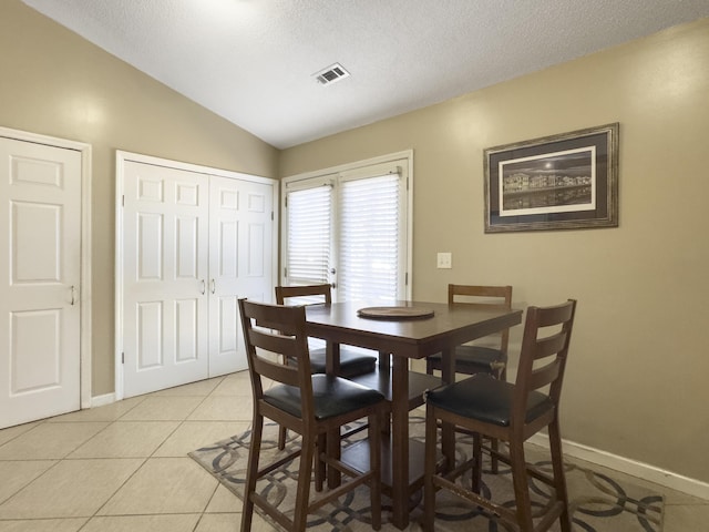 dining area with visible vents, light tile patterned flooring, vaulted ceiling, a textured ceiling, and baseboards