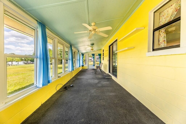 unfurnished sunroom with a wealth of natural light, a ceiling fan, and concrete block wall