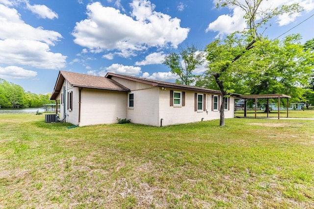 view of side of home with a carport, cooling unit, concrete block siding, and a lawn