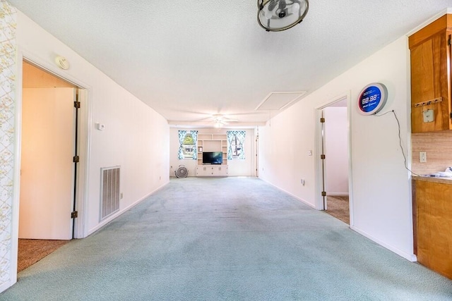 unfurnished living room with visible vents, attic access, a ceiling fan, and carpet
