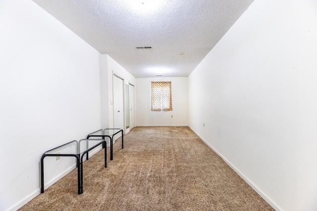 corridor with a textured ceiling, visible vents, baseboards, and carpet floors