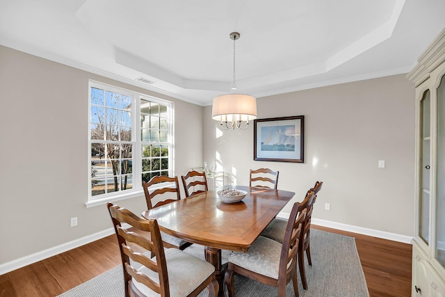 dining room with a raised ceiling, visible vents, baseboards, and wood finished floors