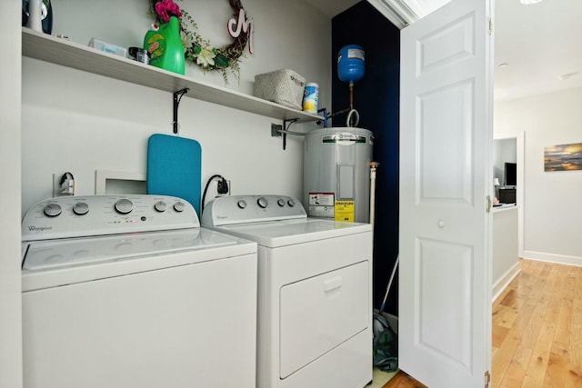 clothes washing area with electric water heater, washer and dryer, and light wood-type flooring