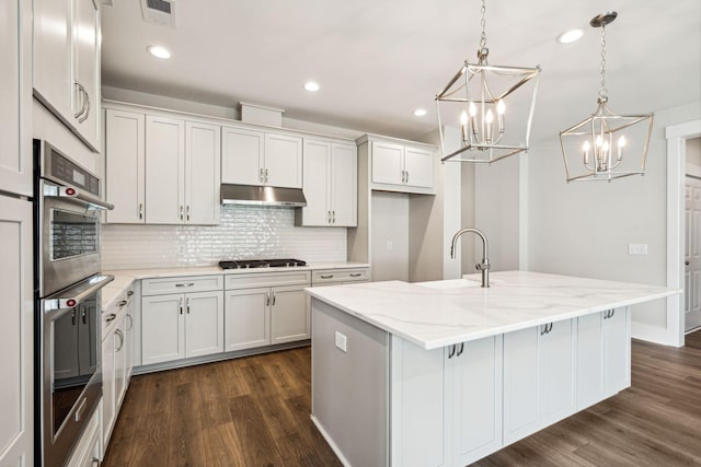 kitchen with a kitchen island with sink, dark hardwood / wood-style floors, sink, decorative light fixtures, and white cabinets