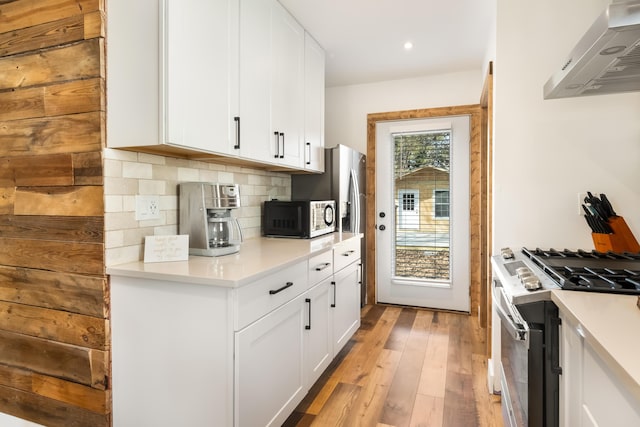 kitchen with white cabinets, decorative backsplash, stainless steel range with gas stovetop, wall chimney range hood, and light hardwood / wood-style flooring