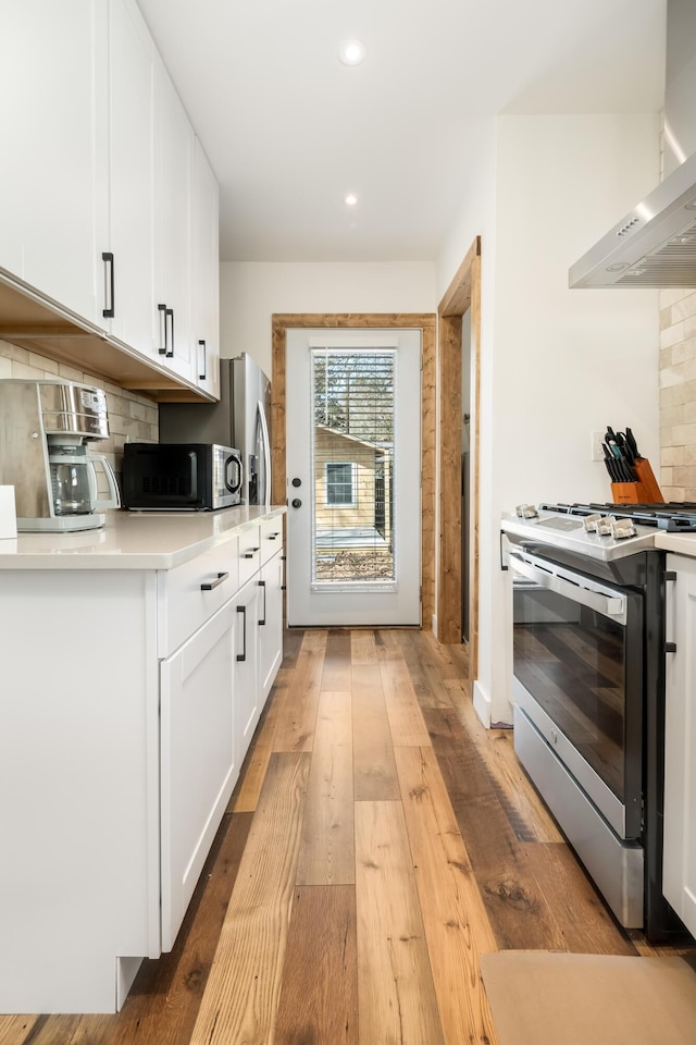 kitchen featuring white cabinetry, appliances with stainless steel finishes, light hardwood / wood-style flooring, and wall chimney exhaust hood