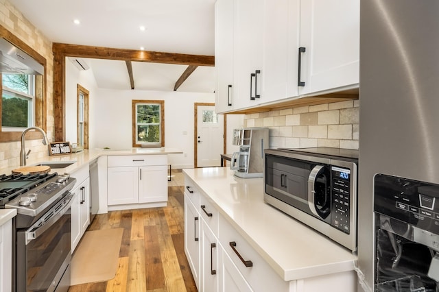 kitchen featuring appliances with stainless steel finishes, beamed ceiling, white cabinets, decorative backsplash, and light wood-type flooring