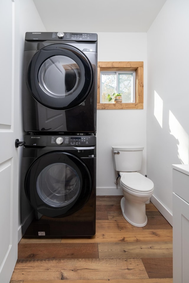 bathroom featuring stacked washer / dryer, hardwood / wood-style floors, and toilet