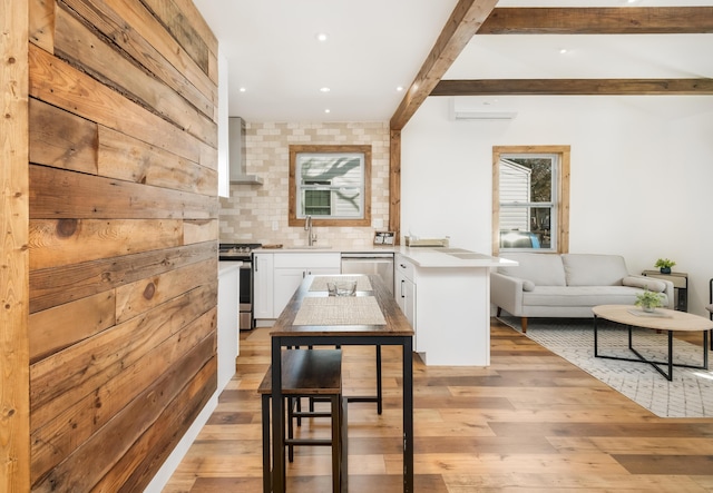 kitchen with appliances with stainless steel finishes, sink, white cabinets, beam ceiling, and wall chimney exhaust hood