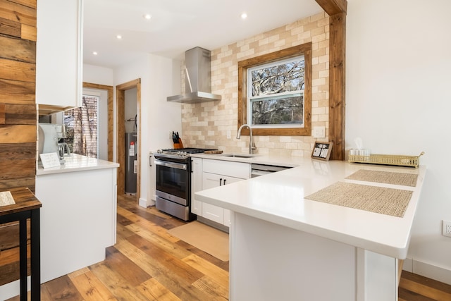 kitchen with sink, a kitchen bar, kitchen peninsula, stainless steel gas range, and wall chimney exhaust hood