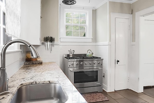 kitchen featuring a sink, high end stainless steel range, dark tile patterned floors, crown molding, and decorative backsplash