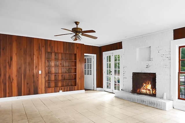 unfurnished living room featuring a ceiling fan, a wealth of natural light, a brick fireplace, and wood walls