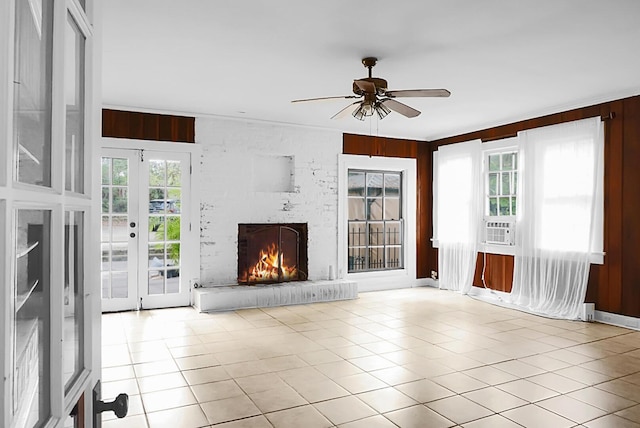 unfurnished living room featuring tile patterned flooring, wood walls, a brick fireplace, and a ceiling fan