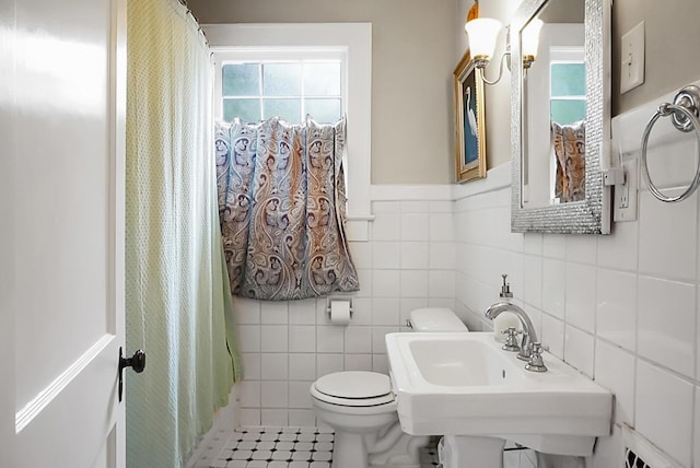 full bath featuring toilet, a sink, a shower with shower curtain, tile walls, and tile patterned flooring