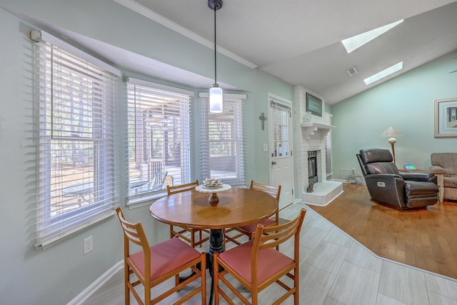 dining room featuring baseboards, vaulted ceiling with skylight, visible vents, a brick fireplace, and wood finished floors