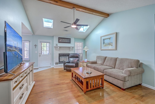 living area featuring visible vents, light wood finished floors, baseboards, a fireplace, and vaulted ceiling with skylight
