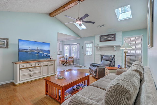 living area featuring light wood-style flooring, visible vents, a fireplace, ceiling fan, and vaulted ceiling with skylight