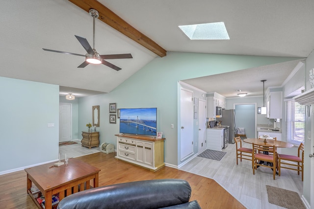 living area with a ceiling fan, light wood-style floors, baseboards, and vaulted ceiling with skylight