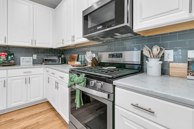 kitchen with light hardwood / wood-style flooring, decorative backsplash, light stone countertops, appliances with stainless steel finishes, and white cabinetry