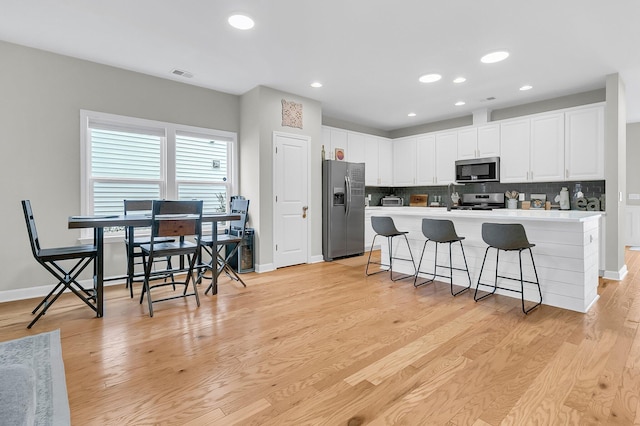 kitchen featuring a breakfast bar area, decorative backsplash, light wood-type flooring, white cabinetry, and stainless steel appliances