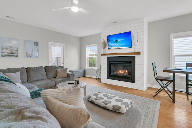 living room with wood-type flooring, a large fireplace, and ceiling fan