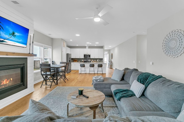 living room featuring ceiling fan, a large fireplace, and light wood-type flooring