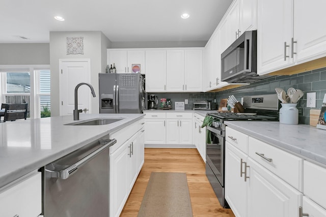 kitchen with decorative backsplash, stainless steel appliances, sink, white cabinets, and light hardwood / wood-style floors