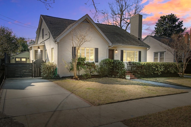 view of front of house with brick siding, roof with shingles, a gate, a chimney, and a front yard