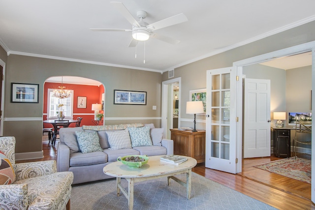 living room with arched walkways, ceiling fan with notable chandelier, wood finished floors, visible vents, and crown molding