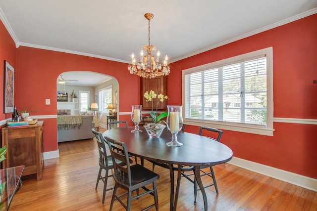 dining area featuring light wood-style floors, arched walkways, crown molding, and a fireplace