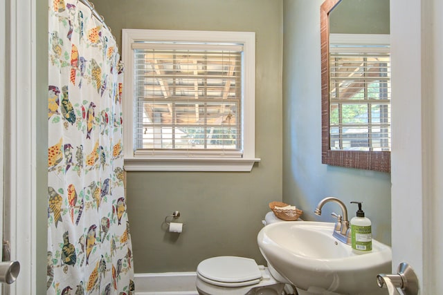 bathroom featuring curtained shower, a sink, toilet, and a healthy amount of sunlight