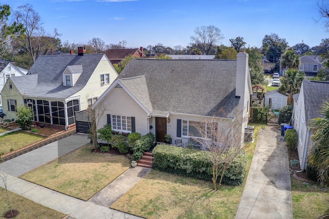 view of front of property with a shingled roof, a front yard, a sunroom, and a chimney