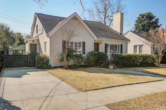 view of front of property with a shingled roof, a front yard, a gate, and brick siding