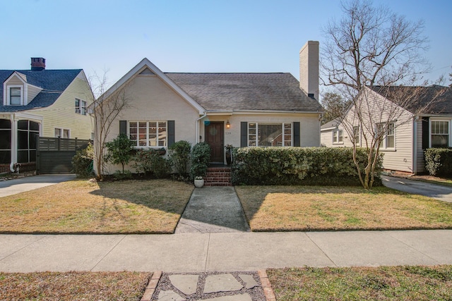 view of front of home with a shingled roof, brick siding, fence, a front lawn, and a chimney