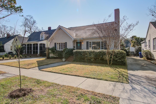 view of front facade featuring fence, driveway, stucco siding, a front lawn, and a chimney