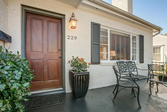 property entrance with a porch, a chimney, and brick siding