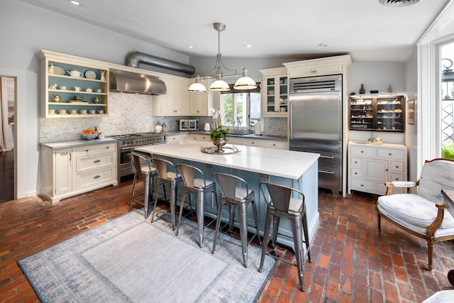 kitchen with hanging light fixtures, high end appliances, tasteful backsplash, wall chimney range hood, and a center island