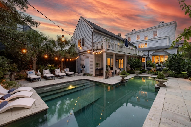 back house at dusk with an outdoor living space, a balcony, and a patio area